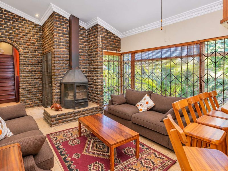 Spacious living room featuring a prominent exposed brick fireplace, vaulted ceilings with crown molding, and large windows with security gates.