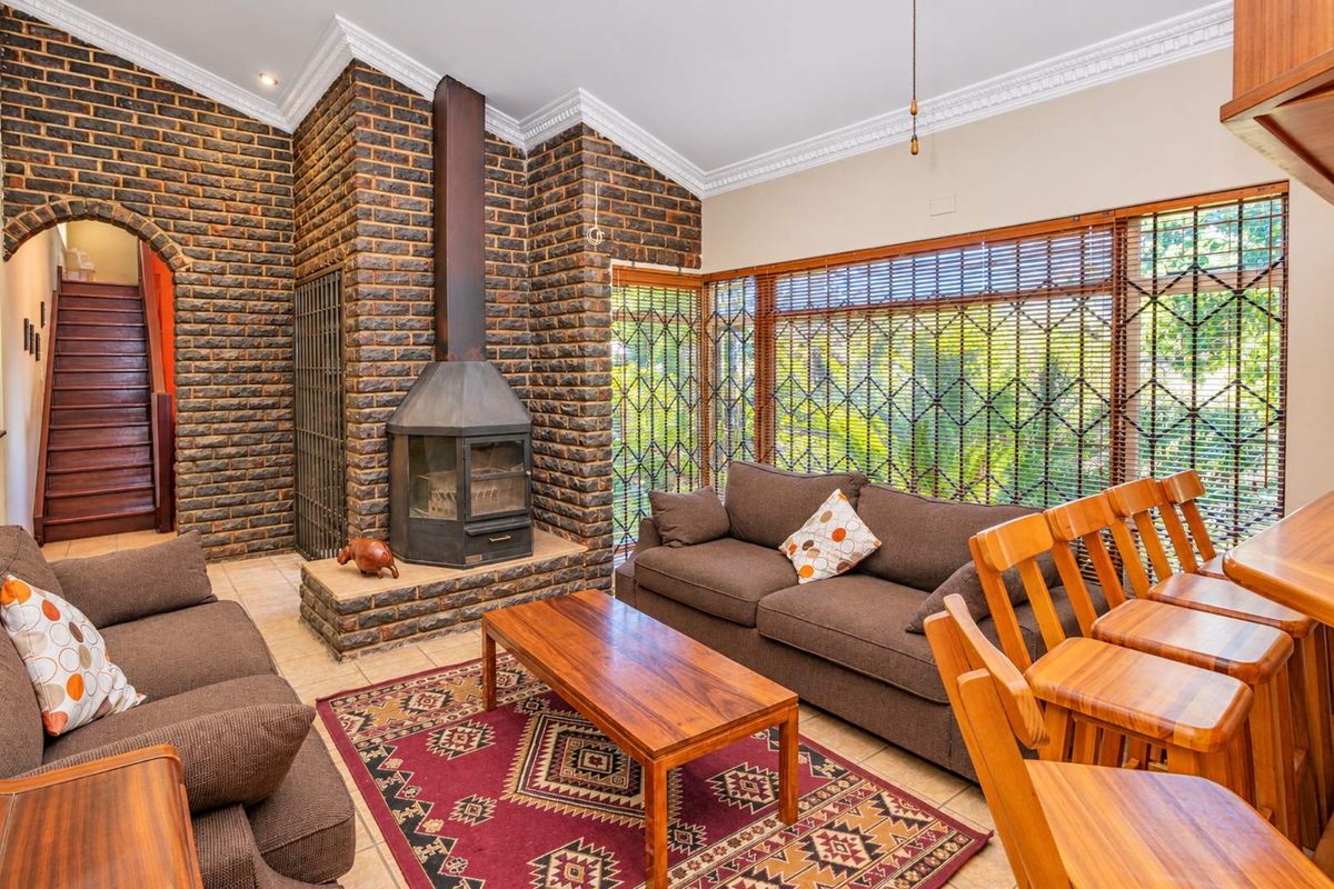 Spacious living room featuring a prominent exposed brick fireplace, vaulted ceilings with crown molding, and large windows with security gates.