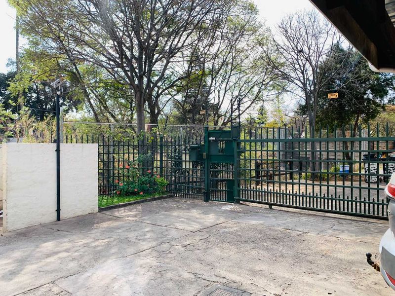 Front entrance view of the property featuring a metal security gate, concrete driveway, and perimeter fencing.