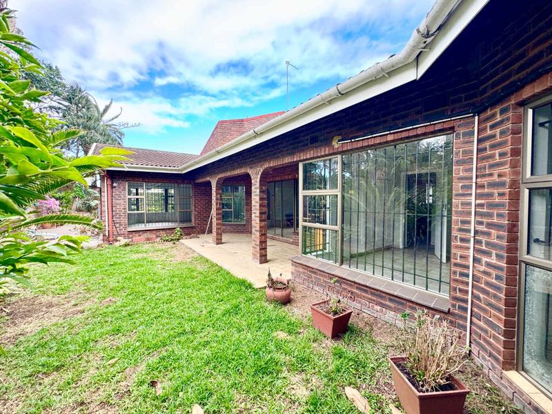 Rear view of the house featuring a brick facade, covered patio area, and large windows with security bars overlooking the garden.