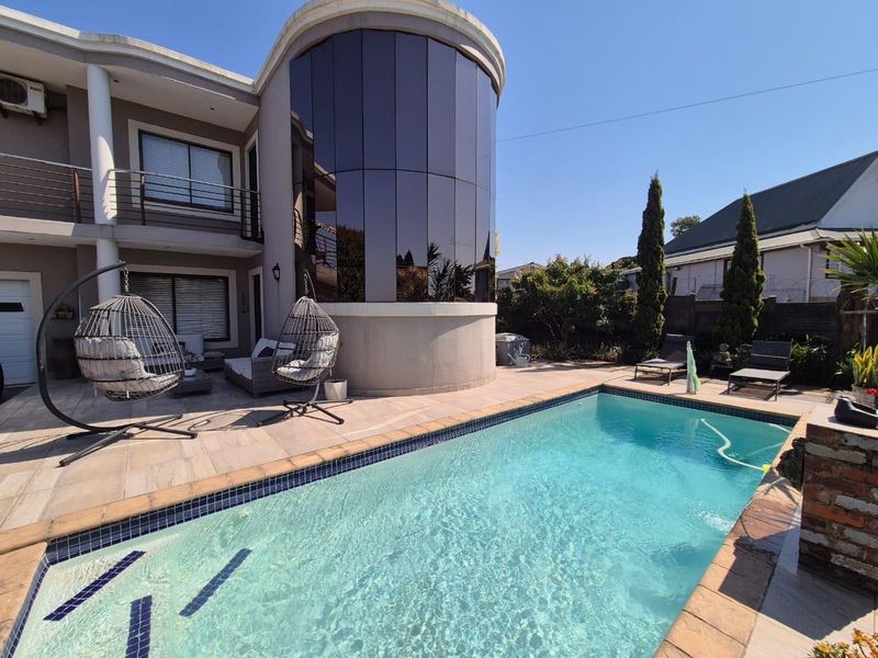 A well-maintained outdoor pool area featuring a tiled patio, a striking curved glass architectural feature, and a clear swimming pool.