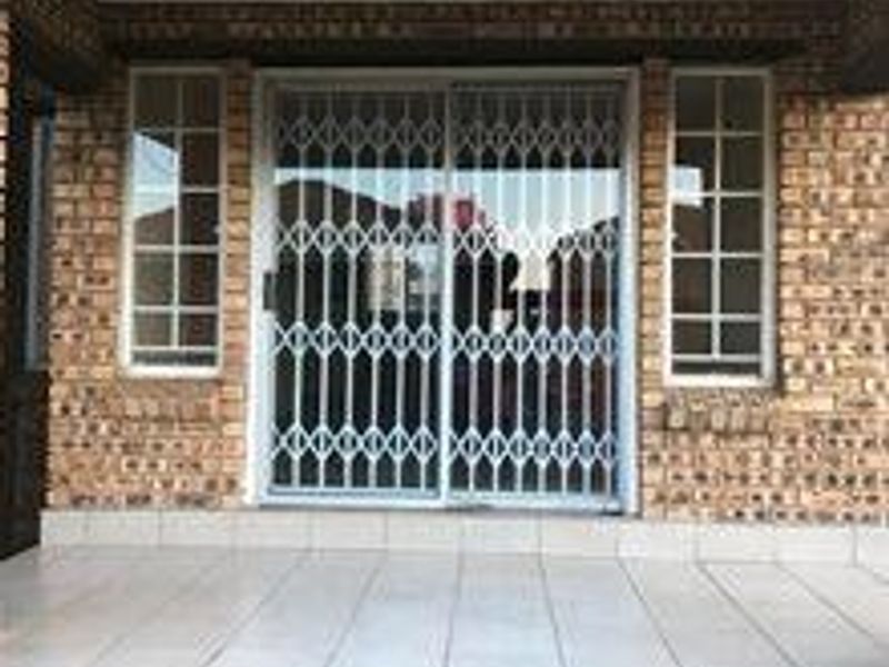 A covered patio area featuring tiled flooring, a brick facade, and a sliding glass door secured with a metal security gate.
