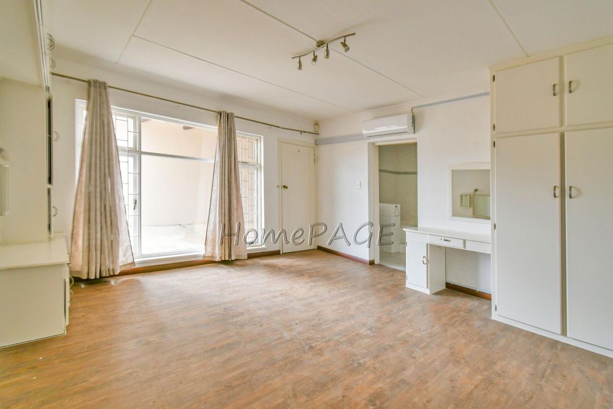 Spacious bedroom featuring built-in cupboards, a vanity unit, air conditioning, and large windows providing natural light and access to an outdoor area.