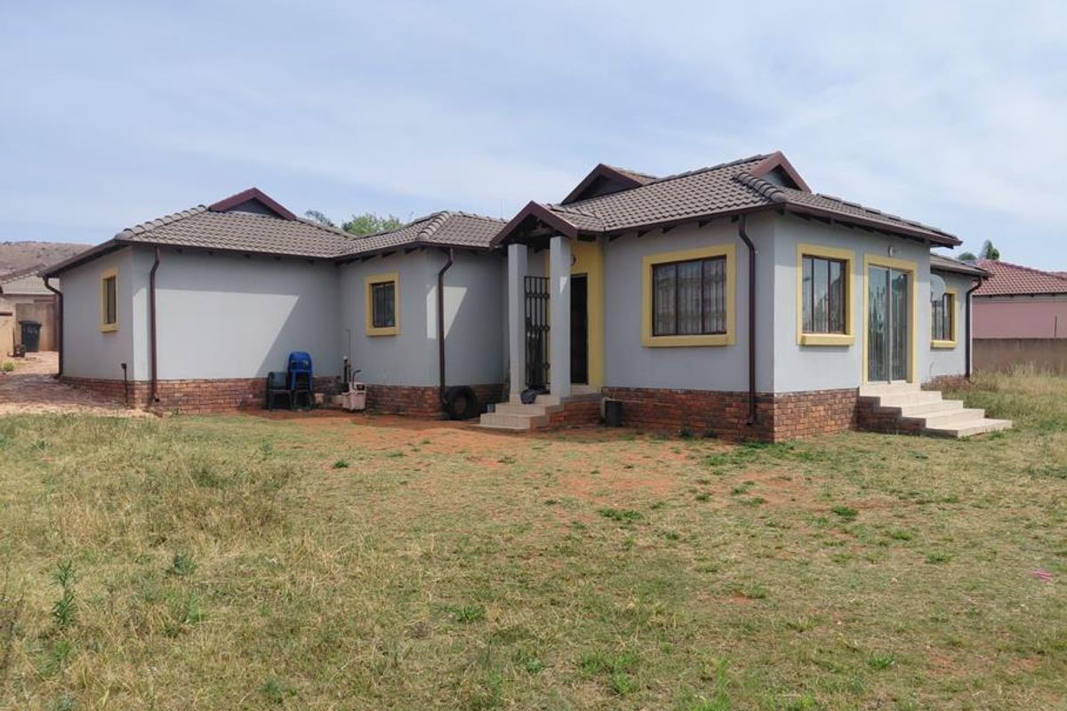 Rear view of a single-story house featuring a tiled roof, brick base, and sliding door access to the yard.