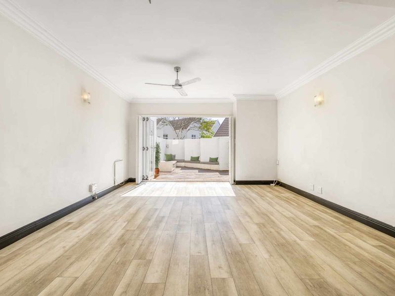 Spacious, light-filled living area featuring modern laminate flooring, crown molding, and bi-fold doors opening onto a private outdoor patio.