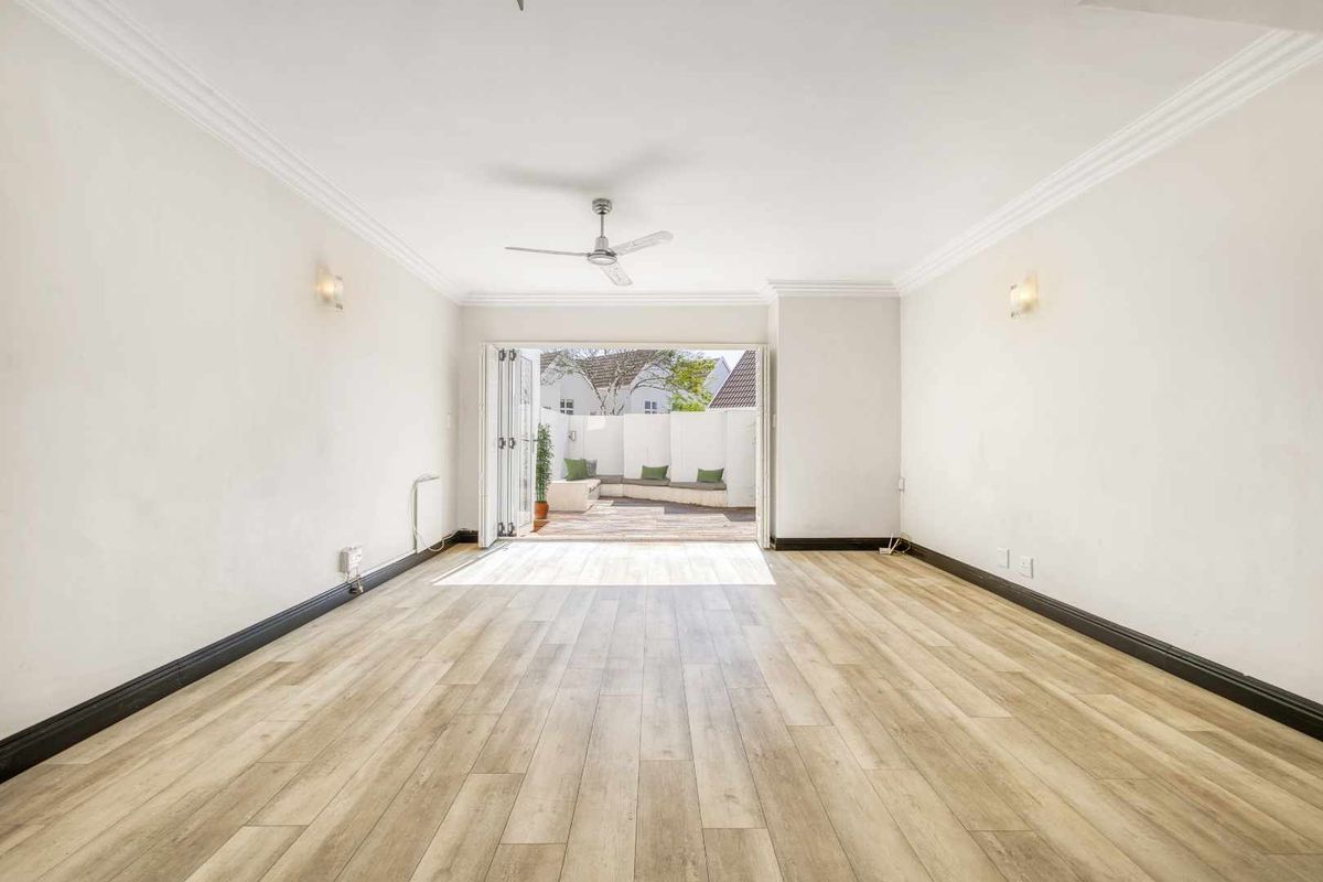 Spacious, light-filled living area featuring modern laminate flooring, crown molding, and bi-fold doors opening onto a private outdoor patio.