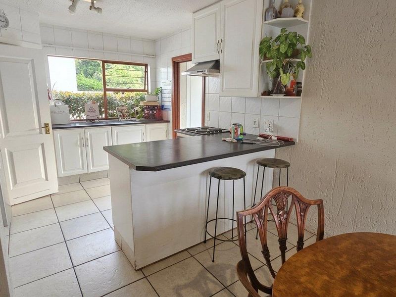 A functional kitchen featuring white cabinetry, a breakfast bar, tiled backsplash, and tiled flooring, offering a practical layout for daily meal preparation.