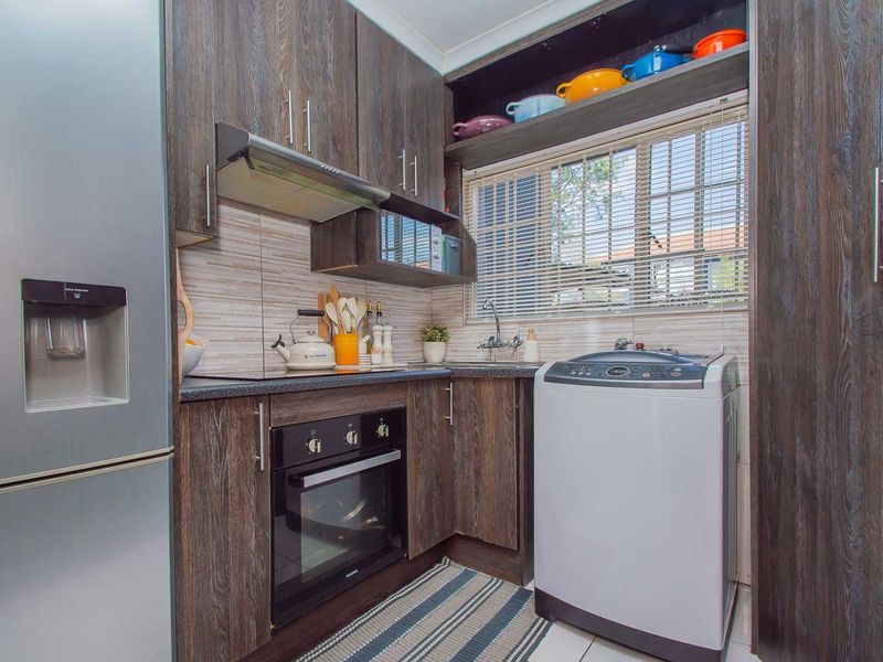 Compact kitchen featuring dark wood-grain cabinetry, built-in oven, extractor fan, and integrated sink with tiled backsplash and window blinds.