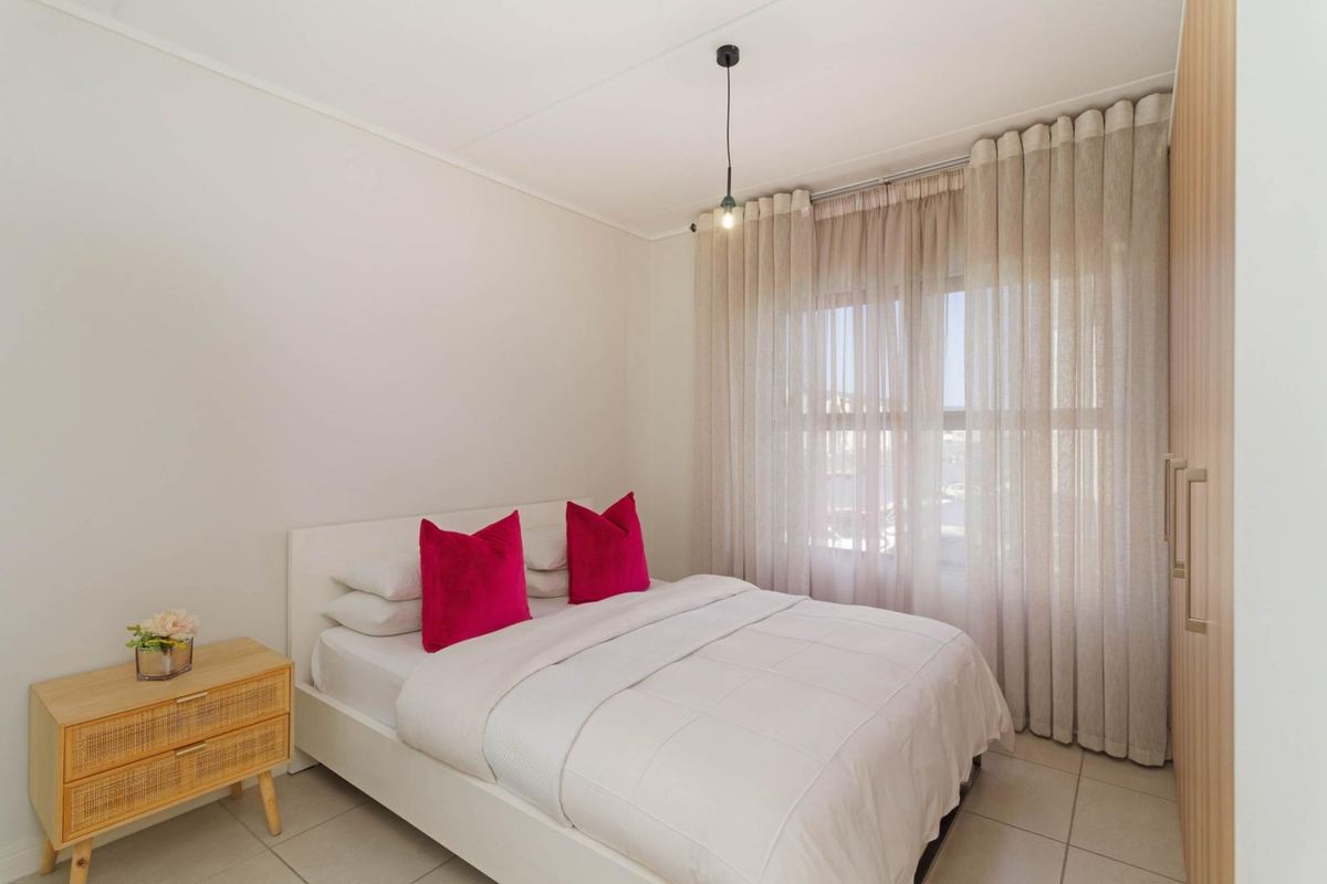 A bright bedroom featuring neutral tiled flooring, a built-in wardrobe, and a large window dressed with floor-to-ceiling curtains.