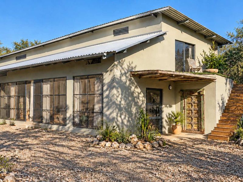 A two-story house featuring a corrugated metal roof, steel-framed windows, a decorative carved wooden door, and an external timber staircase leading to an upper balcony.