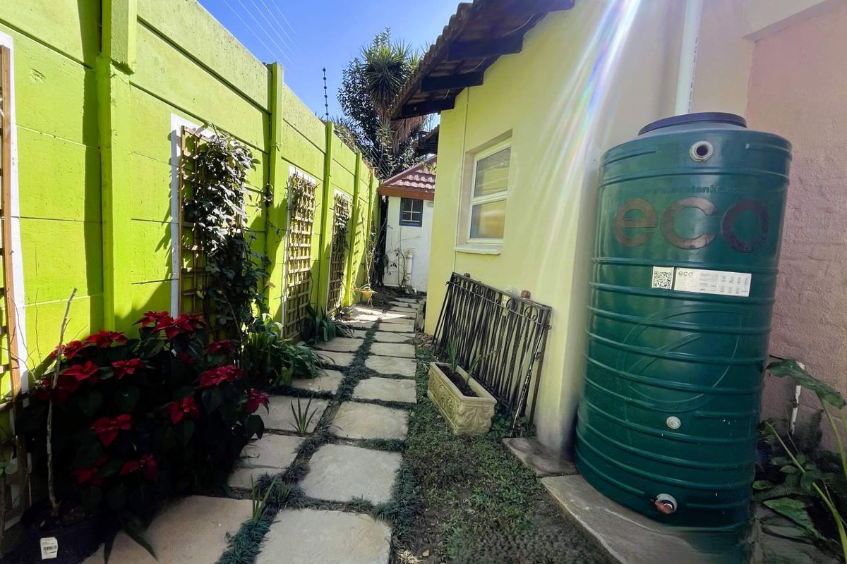 A side garden pathway featuring stone pavers, a large water storage tank, and a precast concrete boundary wall with decorative trellis panels.