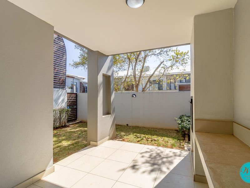 A covered patio featuring tiled flooring, a built-in braai, and a recessed wall niche, overlooking a private garden area.