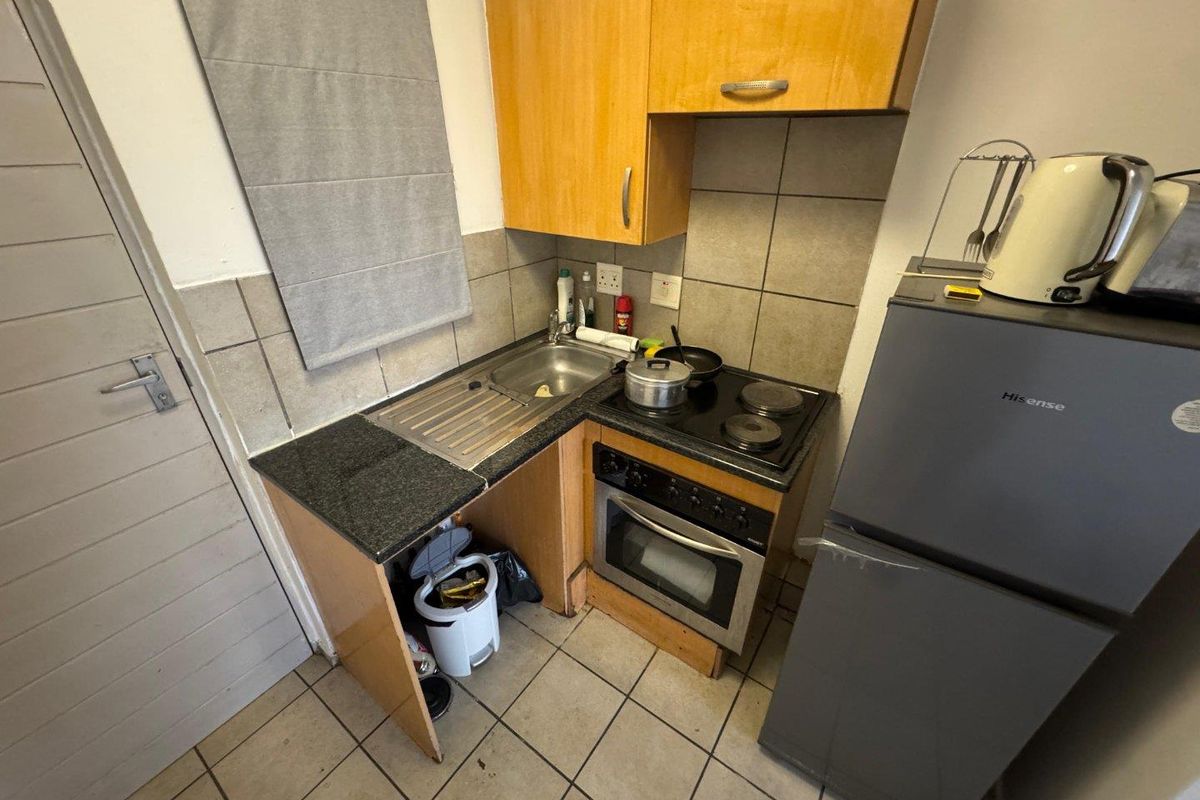 Compact kitchen featuring built-in cabinetry, a stainless steel sink, integrated oven, and electric hob with tiled backsplash.