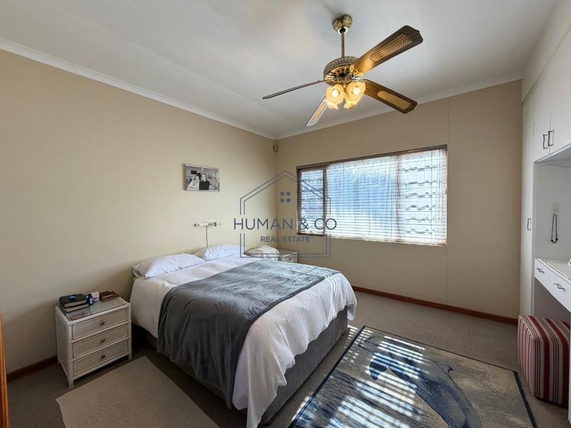 A well-lit bedroom featuring built-in cupboards, a ceiling fan, and carpeted flooring, offering a comfortable and functional living space.