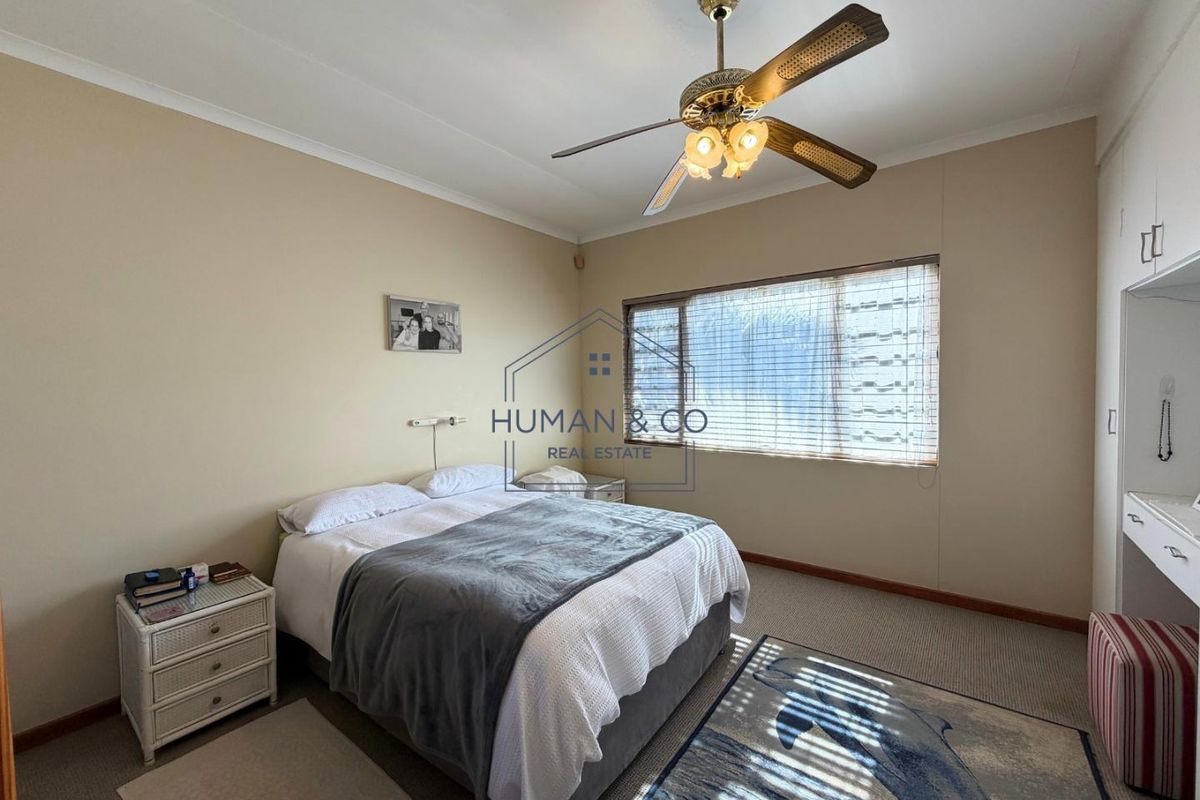 A well-lit bedroom featuring built-in cupboards, a ceiling fan, and carpeted flooring, offering a comfortable and functional living space.