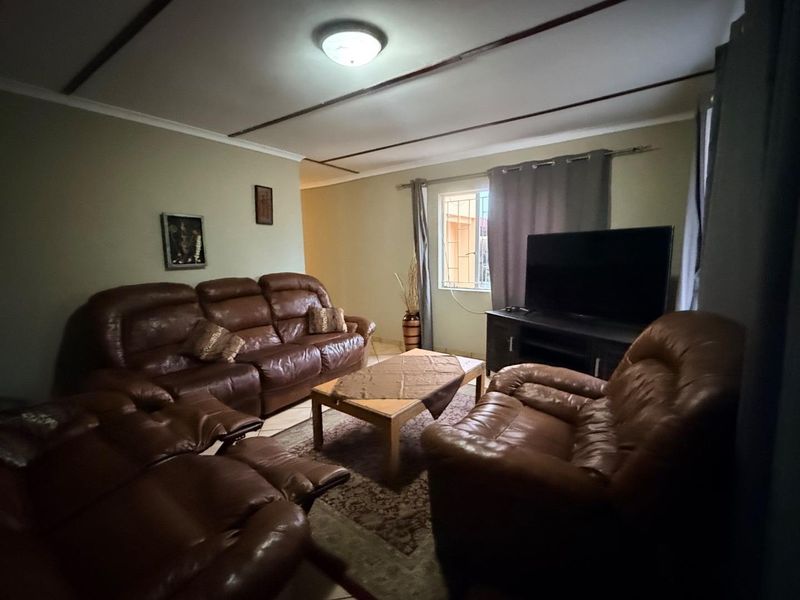 A comfortable living room featuring tiled flooring, ceiling beams, and a window fitted with security bars.