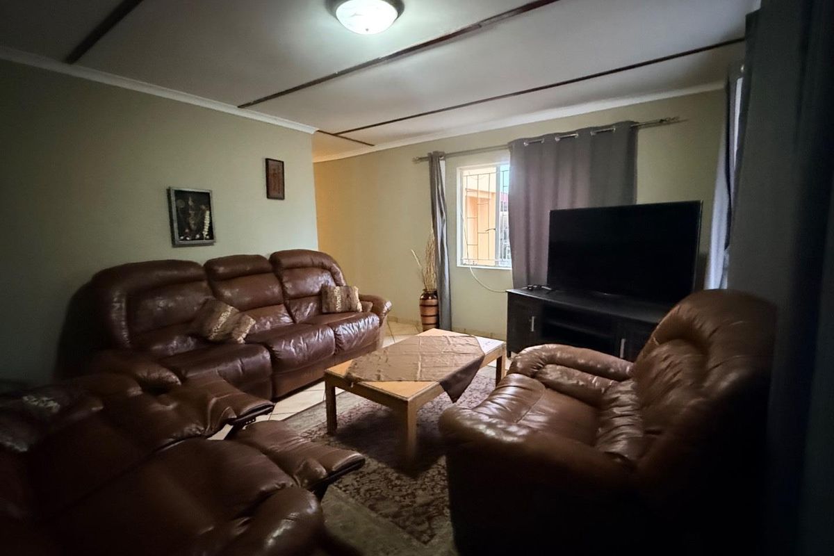 A comfortable living room featuring tiled flooring, ceiling beams, and a window fitted with security bars.