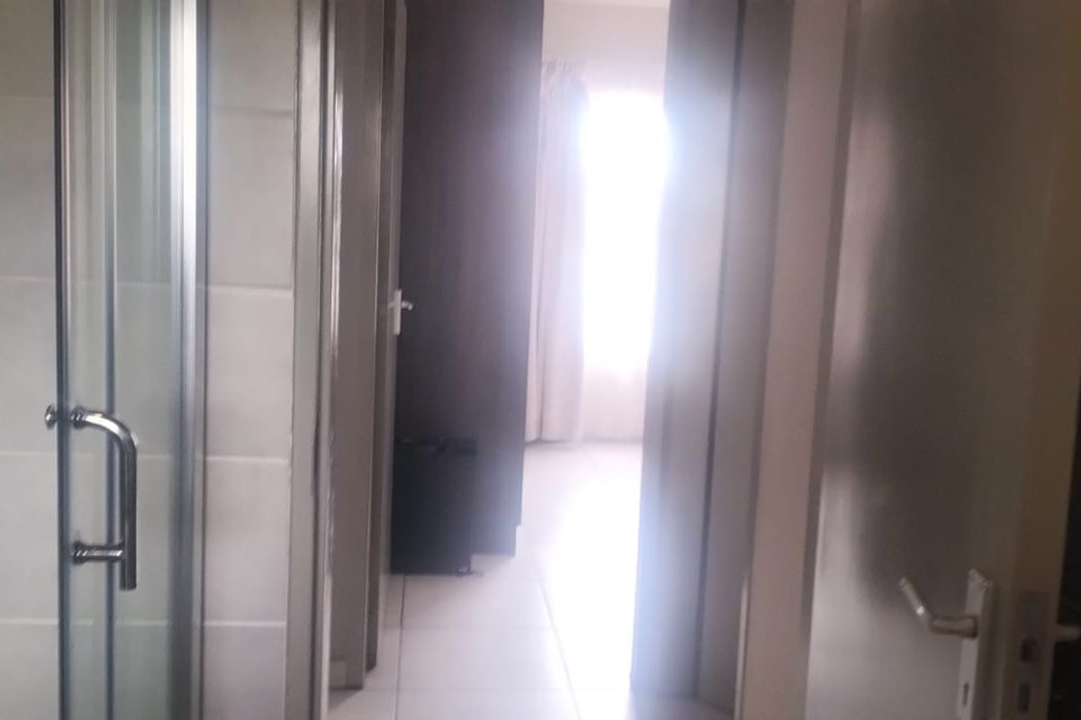 A bathroom featuring a glass shower enclosure with tiled walls and flooring, leading into an adjacent room.