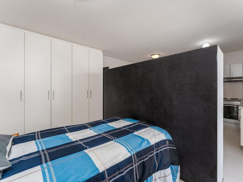 Open plan studio apartment featuring a bedroom area with built-in cupboards and a compact kitchen with modern appliances and tiled flooring.