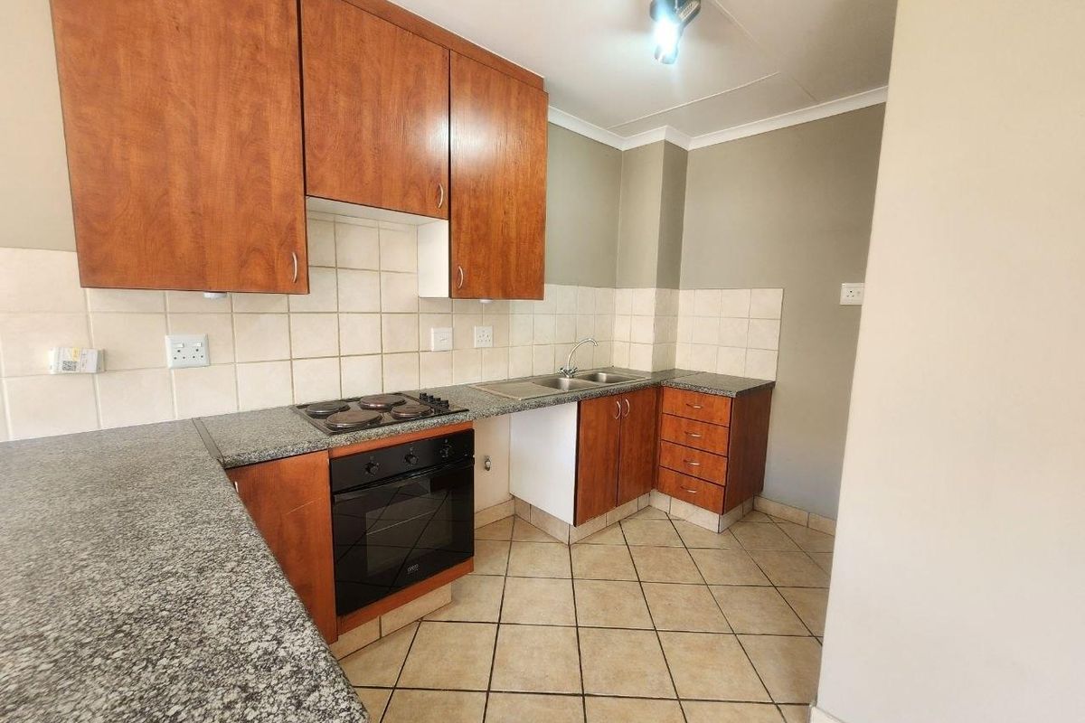 A functional kitchen featuring granite countertops, built-in oven, electric hob, double sink, and ample wooden cabinetry with tiled flooring and backsplash.