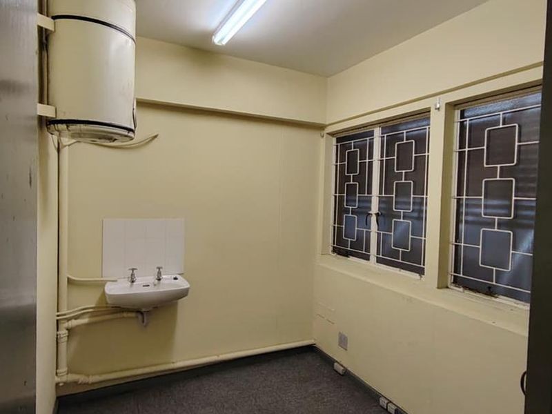A functional utility space featuring a wall-mounted basin, water heater, and security-barred windows, suitable for storage or laundry conversion.