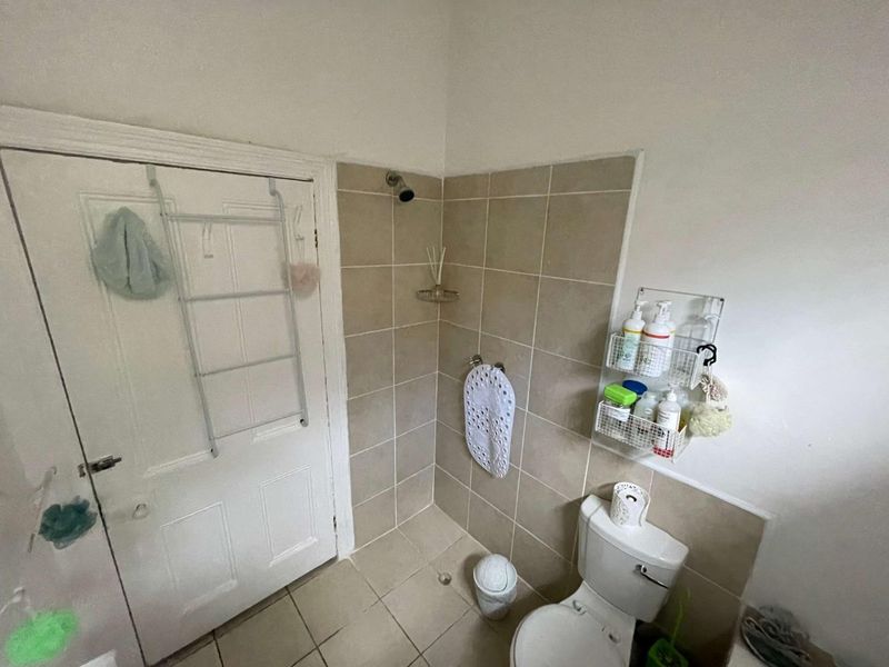 A compact bathroom featuring a shower area with tiled walls, ceramic floor tiling, and a standard toilet.