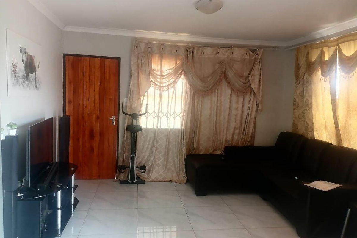 A living room featuring tiled flooring, a solid wood door, and security bars on the windows.