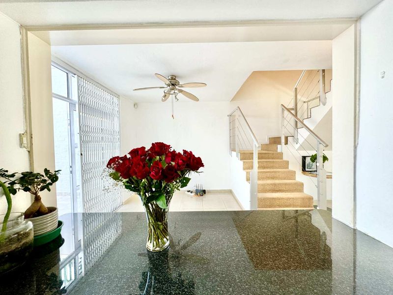 Open plan living area featuring a granite breakfast bar, tiled flooring, ceiling fan, and a staircase with a modern stainless steel balustrade.