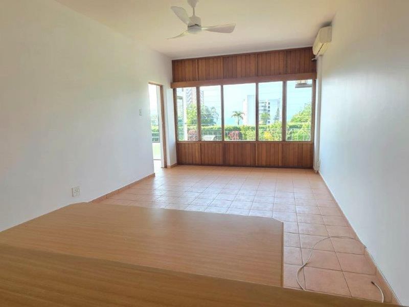 An empty living room featuring tiled flooring, a ceiling fan, and large timber-framed windows providing natural light and exterior views.