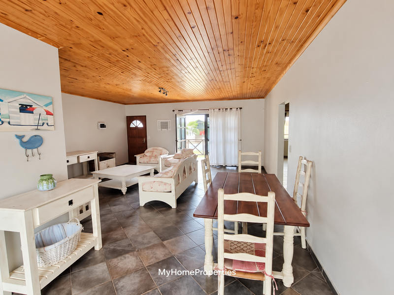 Open plan living and dining area featuring a warm timber tongue and groove ceiling and tiled flooring with direct access to the outdoor space.