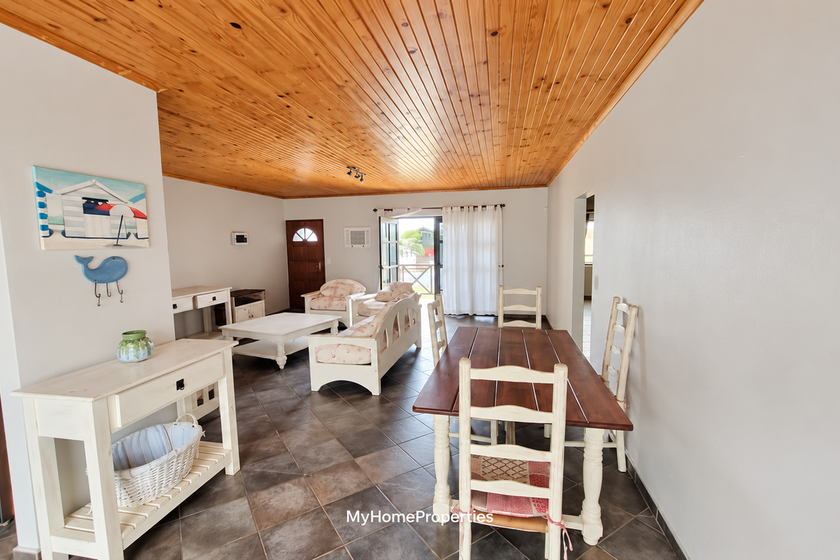 Open plan living and dining area featuring a warm timber tongue and groove ceiling and tiled flooring with direct access to the outdoor space.