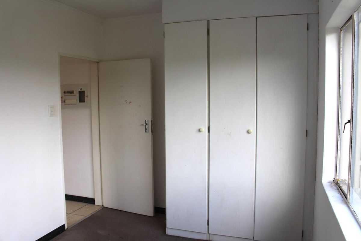 A bedroom featuring built-in cupboards, neutral walls, and carpeted flooring, providing a functional space with direct access to the hallway.