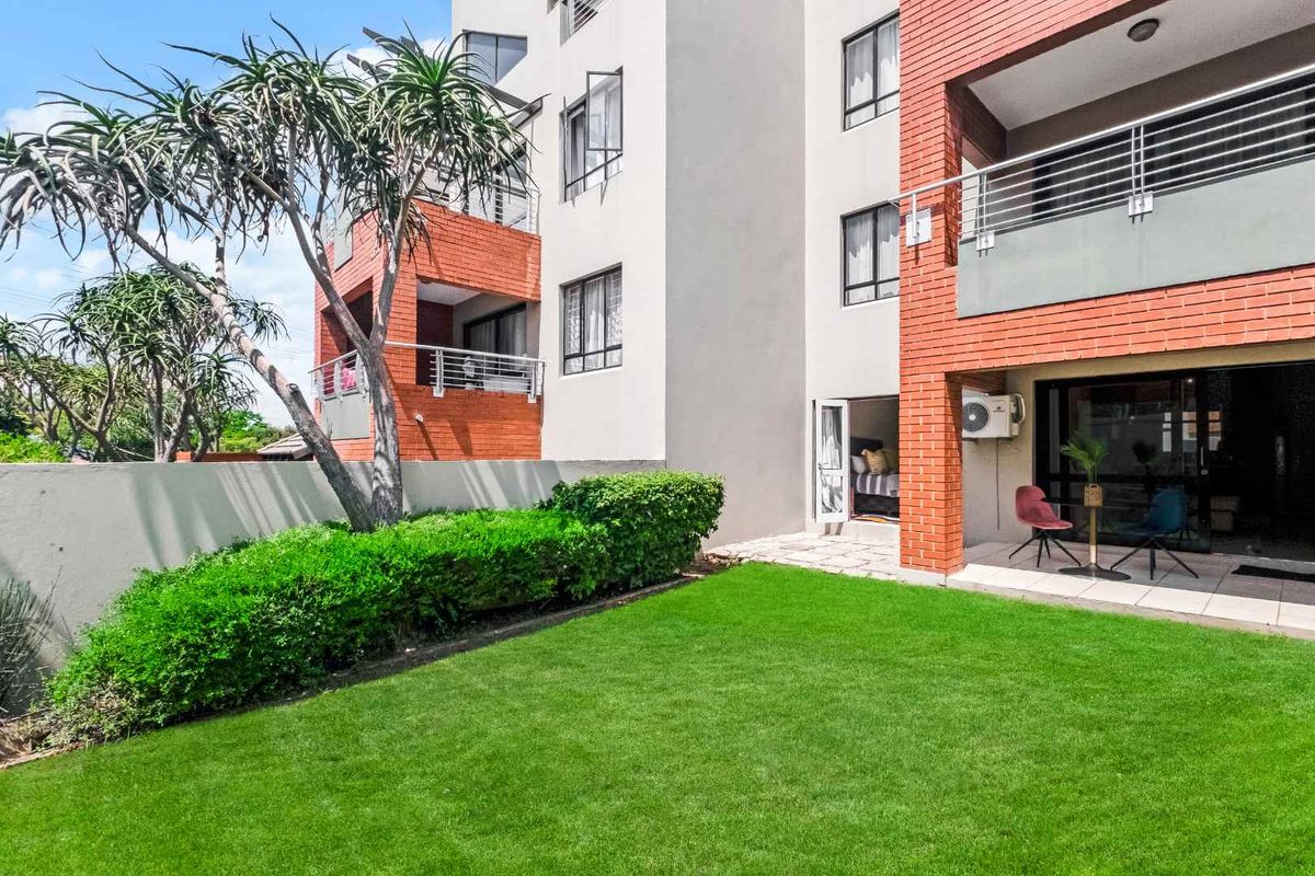 A view of the apartment building exterior featuring a private garden area, paved patio, and brick facade detailing.