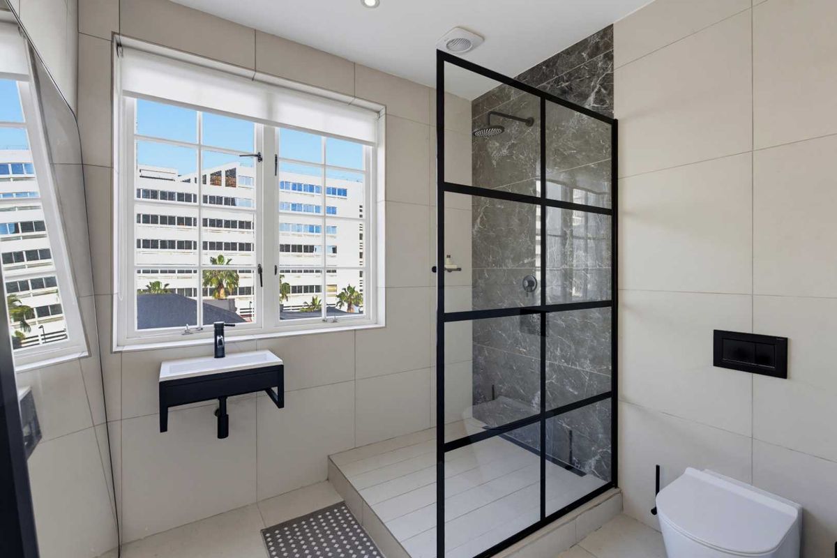 Modern bathroom featuring a walk-in shower with a black-framed glass screen, wall-mounted vanity, and wall-hung toilet with contemporary tiled finishes.