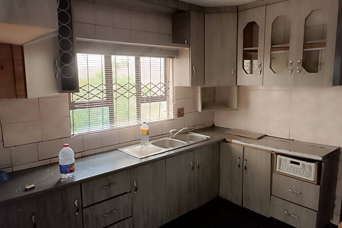 A dated kitchen featuring wood-look cabinetry, a double-basin stainless steel sink, and tiled splashbacks, offering potential for a modern renovation.