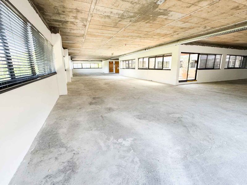 Spacious open-plan office area featuring an industrial aesthetic with exposed concrete ceilings, large windows, and natural light, suitable for a modern workspace fit-out.