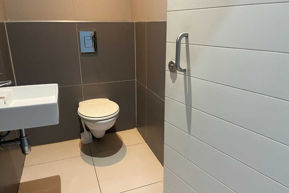 A modern bathroom featuring a wall-mounted toilet with a concealed cistern, a sleek basin, and neutral-toned floor and wall tiling.