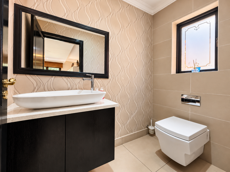 Modern bathroom featuring a floating vanity with a vessel sink, wall-mounted toilet, and elegant patterned wallpaper with neutral wall tiles.
