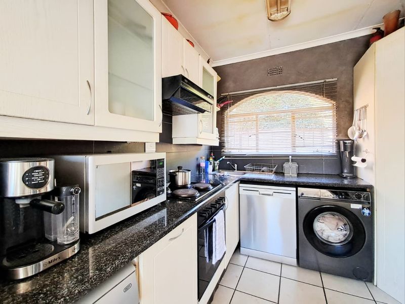 Compact kitchen featuring granite countertops, built-in cabinetry, electric hob, oven, and integrated dishwasher with tiled flooring and a window for natural light.