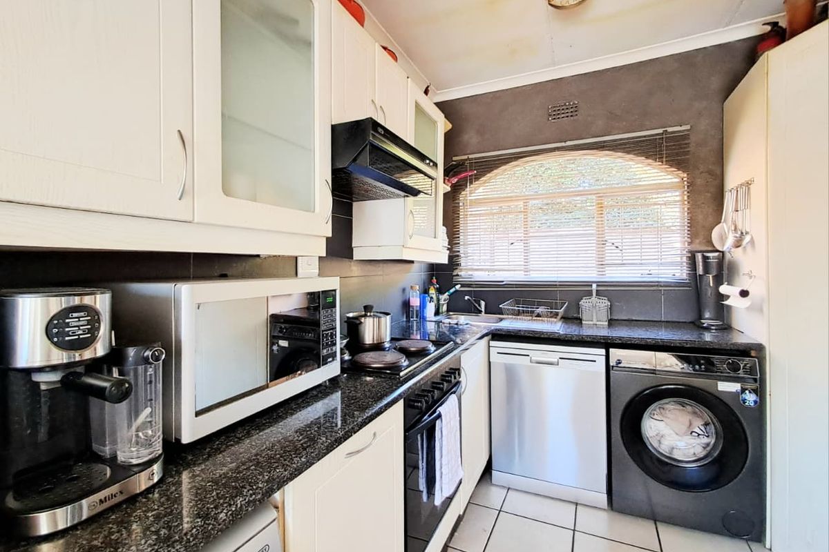 Compact kitchen featuring granite countertops, built-in cabinetry, electric hob, oven, and integrated dishwasher with tiled flooring and a window for natural light.