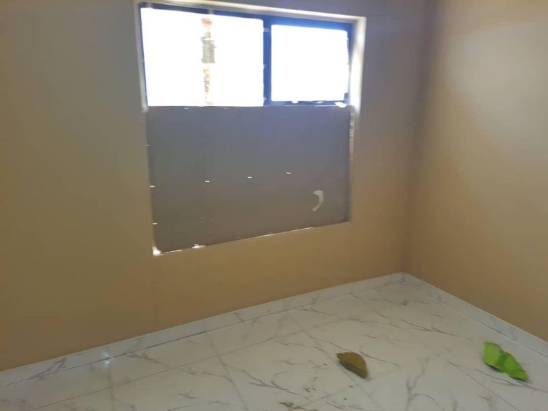 An empty bedroom featuring light-colored marble-effect floor tiles and a window with temporary covering.