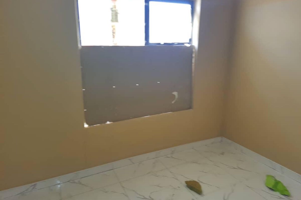 An empty bedroom featuring light-colored marble-effect floor tiles and a window with temporary covering.