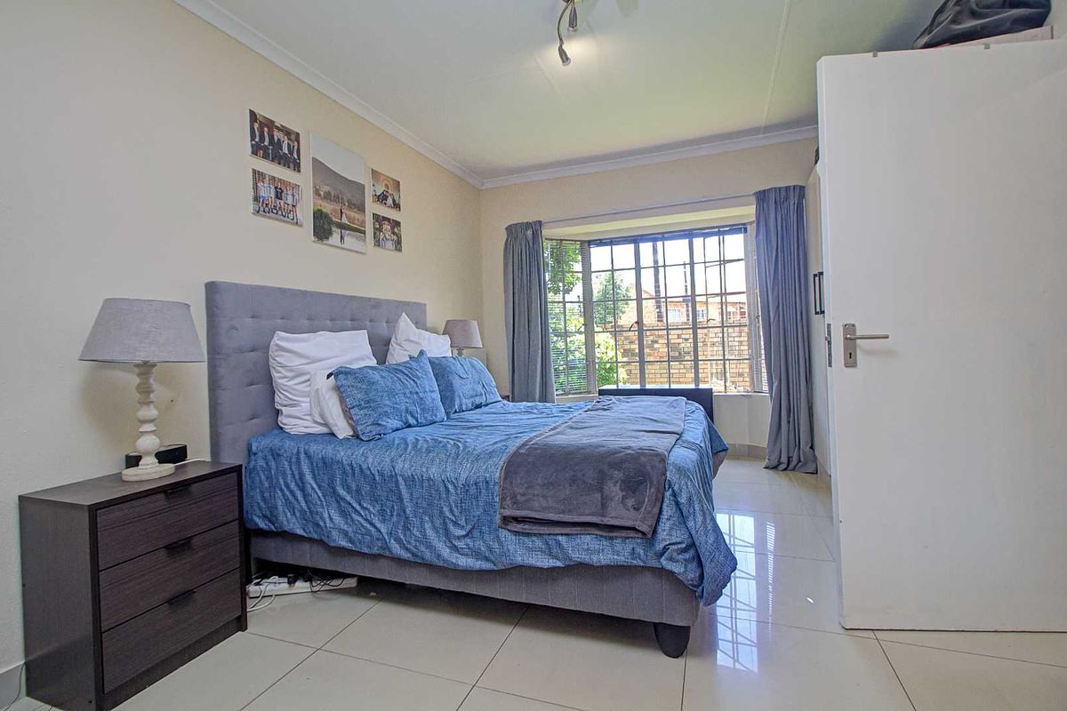 A well-lit bedroom featuring large format floor tiles, a bay window with security bars, and neutral wall finishes.