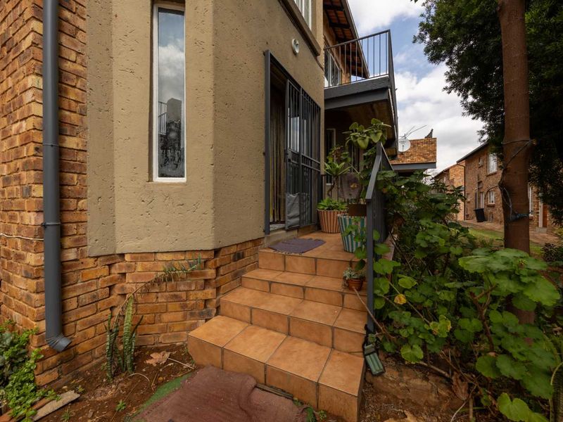 Front entrance of the townhouse featuring tiled steps, a security gate, and brick exterior walling with an overhead balcony.