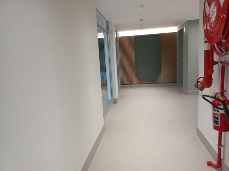 A modern, well-maintained commercial hallway featuring tiled flooring, recessed lighting, and decorative timber slat wall paneling with integrated fire safety equipment.