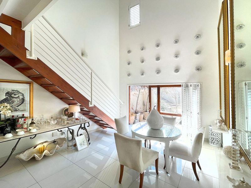 Bright living area featuring high ceilings, a timber staircase with metal balustrade, polished tiled flooring, and sliding glass doors leading to an outdoor space.