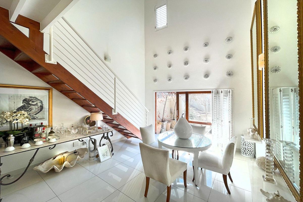 Bright living area featuring high ceilings, a timber staircase with metal balustrade, polished tiled flooring, and sliding glass doors leading to an outdoor space.
