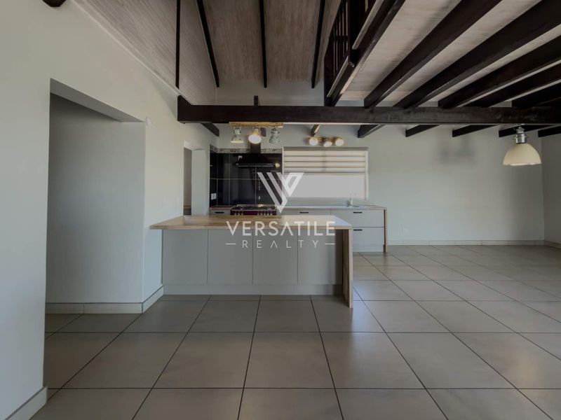 Spacious open-plan kitchen and living area featuring exposed timber ceiling beams, modern cabinetry, a central island, and neutral tiled flooring throughout.