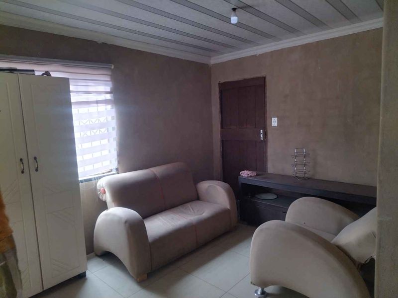 A living room space featuring tiled flooring, a timber door, and unfinished wall plaster, offering potential for renovation and aesthetic improvement.
