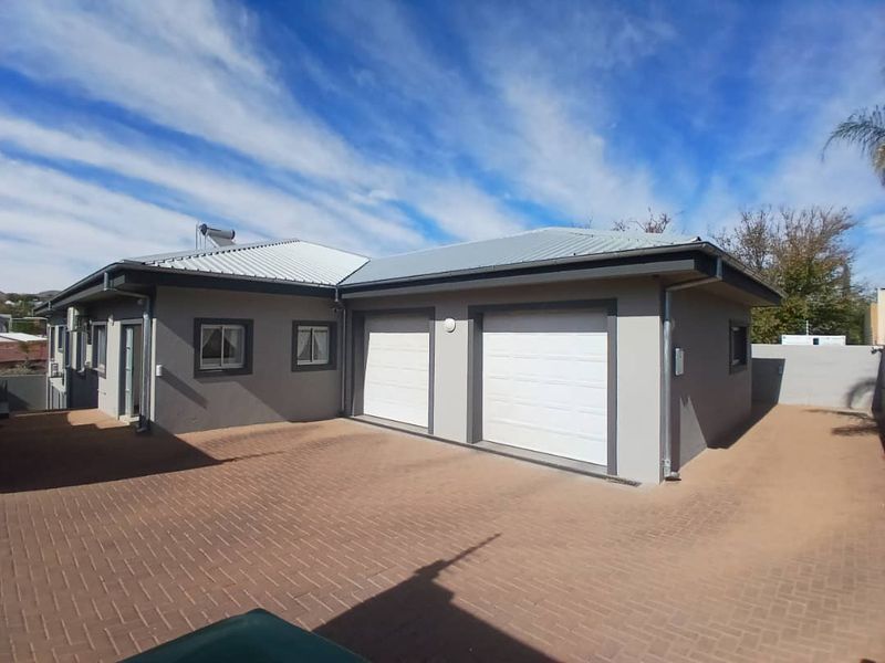 A well-maintained exterior view of a house featuring a double garage, paved driveway, and a metal roof with a solar geyser installation.